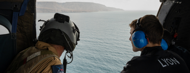 Un Aviateur et un jeune lauréat du BIA en vol basse altitude, porte du PUMA ouverte au-dessus de la mer