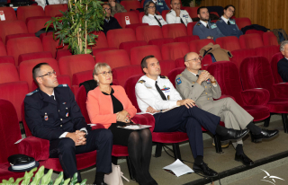 Militaires, réservistes et civils écoutent un orateur dans fauteuils d'un amphithéâtre lors de la conférence.
